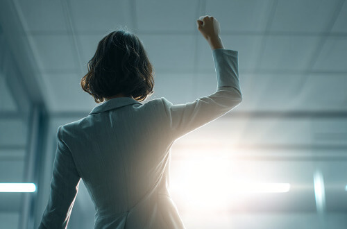 活力あふれる毎日をイメージして、拳を突き上げるビジネスパーソンの後ろ姿