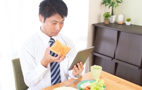 タブレットを見ながら朝食を食べるビジネスマン